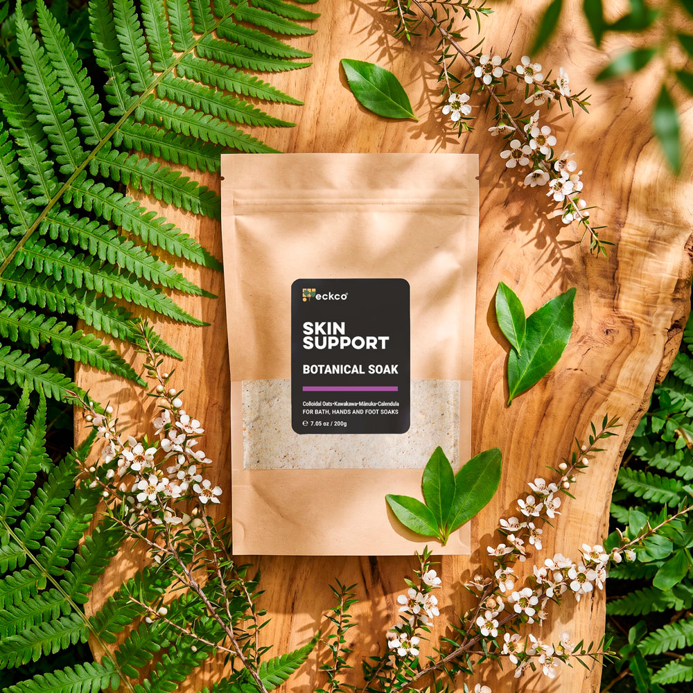 Eckco Skin Support Botanical Soak kraft pouch on rustic wood, surrounded by ferns and flowers.